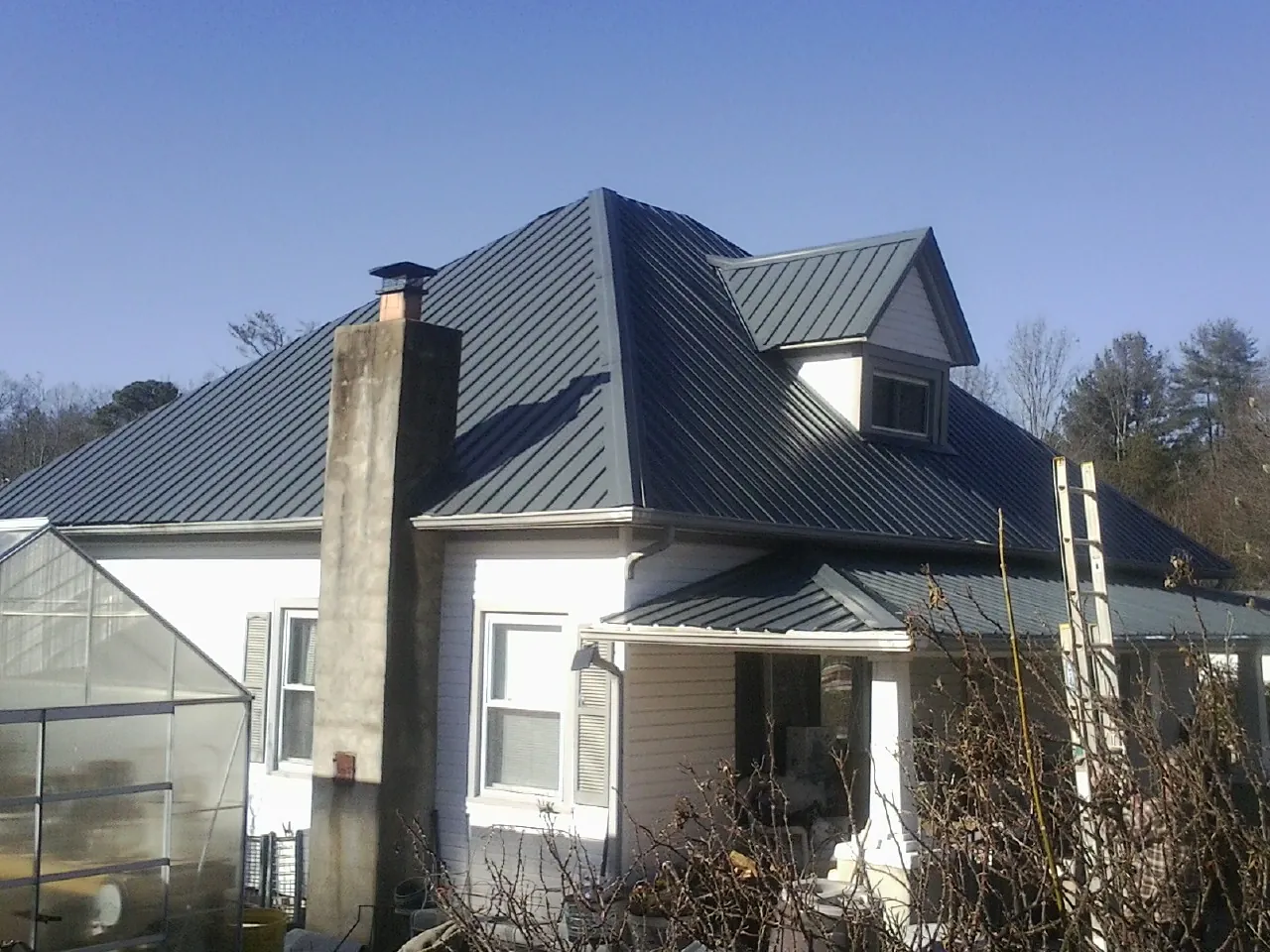Dark blue standing seam metal roof on a white farmhouse with dormer — Slate & Tile Roof Repair by Roofing Brothers in Widen