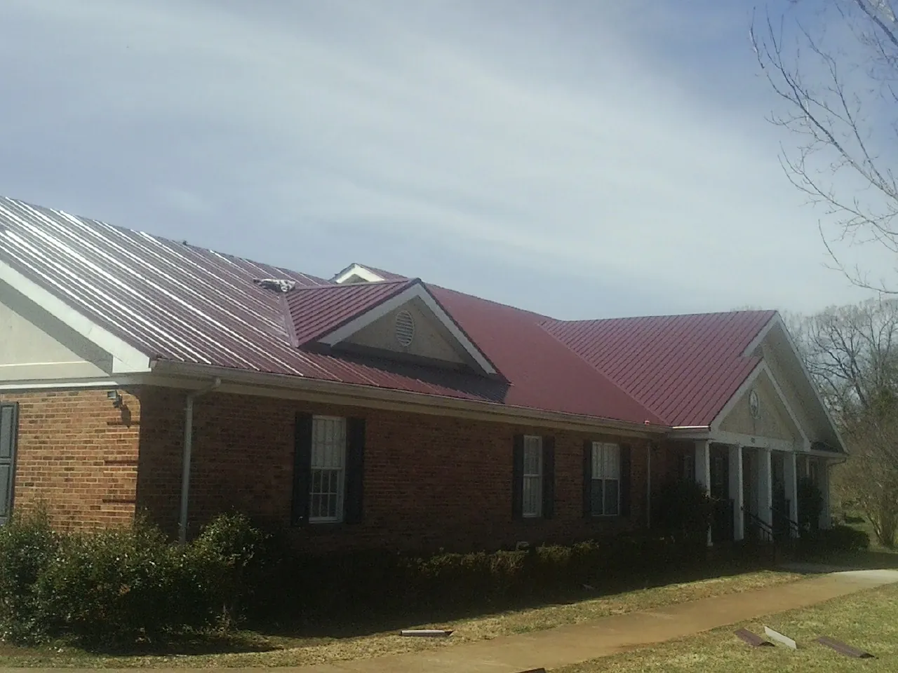 Red metal roof with gabled entries on a long brick building, from a Hail Damage Roof Repair job in Widen