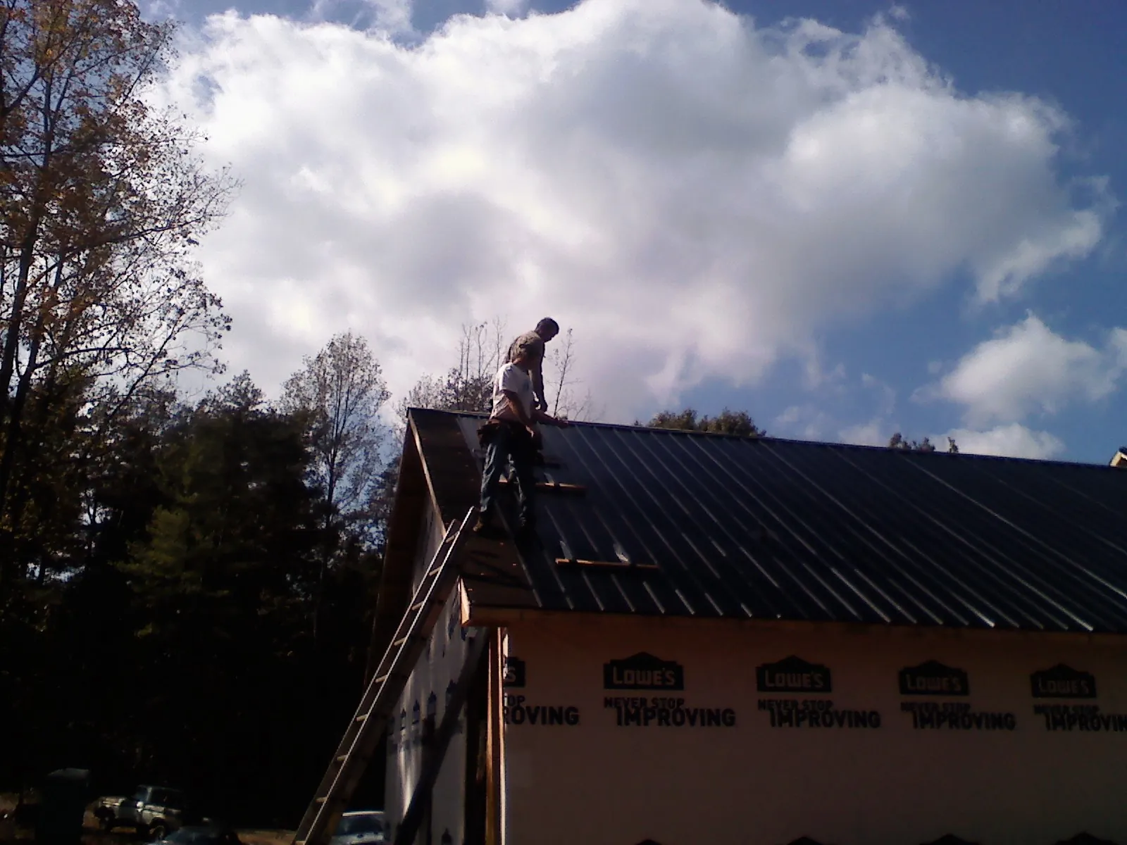Roofer fastening dark metal panels high against a cloudy sky, from a Roof Inspection job in Widen