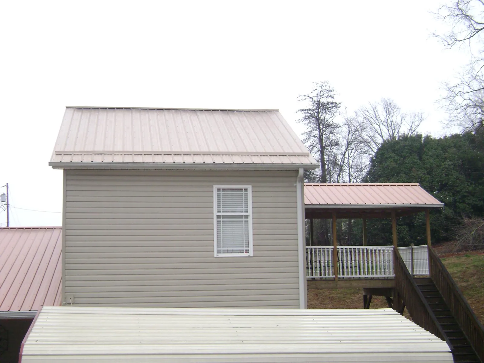 Tan metal roofs on a two story addition and attached porch, from a Roof Replacement job in Widen